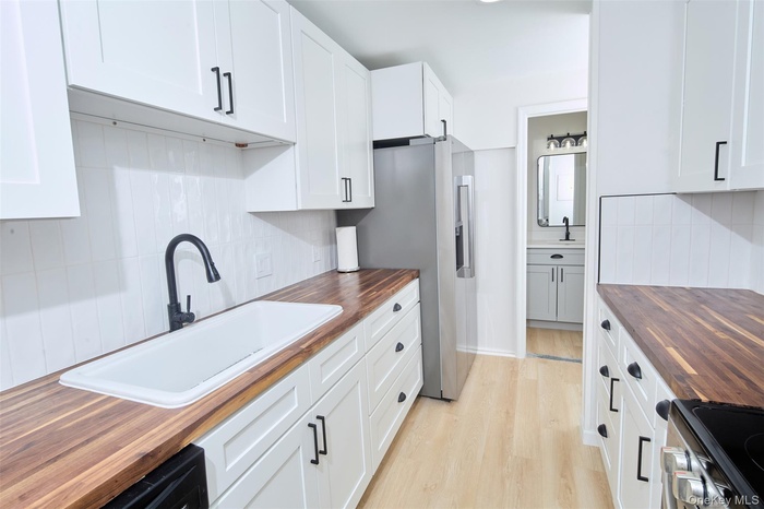 Kitchen featuring butcher block counters, white cabinetry, light wood finished floors, range with electric stovetop, and backsplash