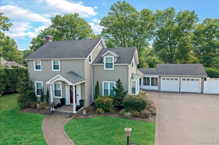 Traditional home featuring an attached garage, driveway, a front lawn, a chimney, and roof with shingles