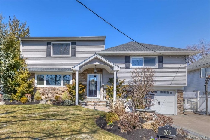 View of front facade with stone siding, an attached garage, a front lawn, concrete driveway, and a shingled roof