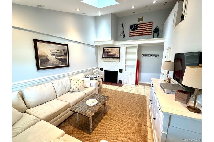 Living area with a skylight, recessed lighting, a fireplace with raised hearth, a high ceiling, and light tile patterned floors
