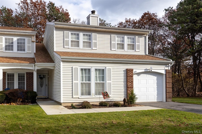 Traditional-style home featuring asphalt driveway, a front lawn, a chimney, an attached garage, and a shingled roof