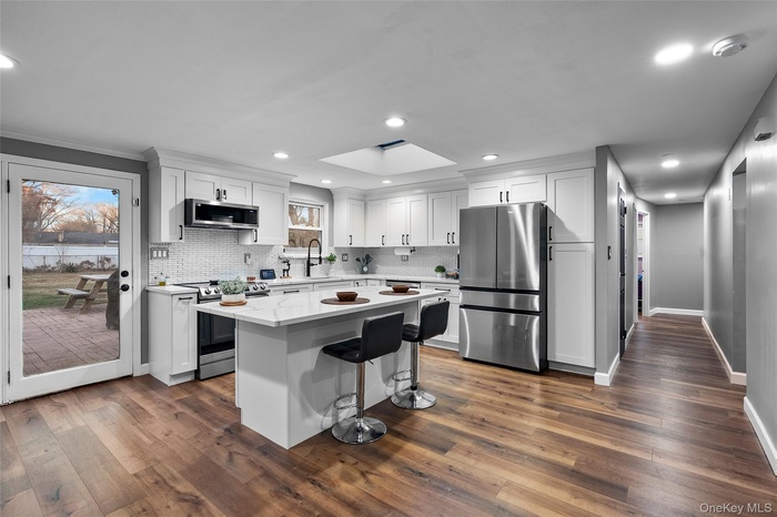 Kitchen featuring a skylight, stainless steel appliances, a kitchen bar, white cabinetry, and dark wood finished floors
