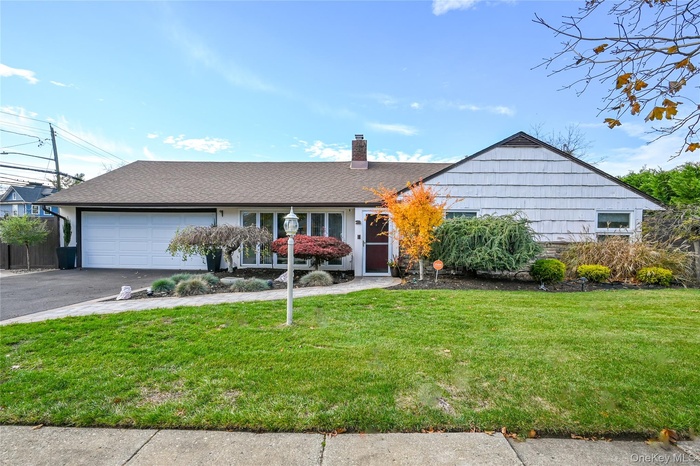 Single story home featuring a front yard, a shingled roof, a chimney, a garage, and driveway