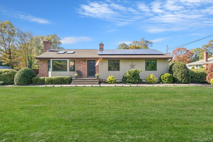 View of front of property featuring roof mounted solar panels, a chimney, and a front lawn