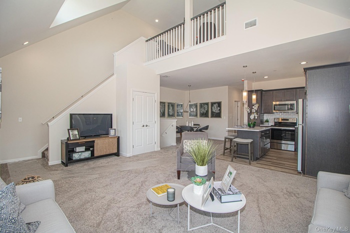 Living area featuring light carpet, stairs, a towering ceiling, and recessed lighting