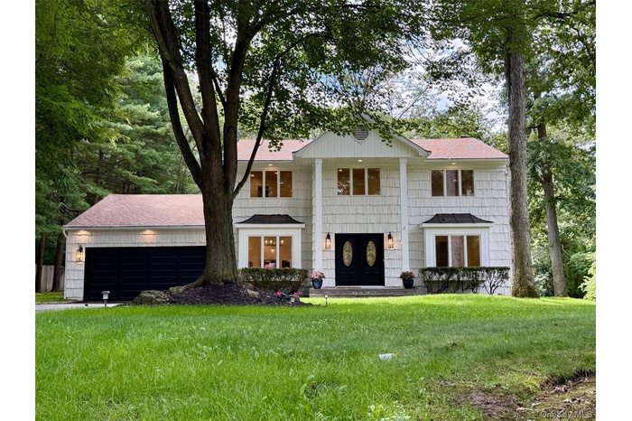 Neoclassical home with an attached garage, roof with shingles, and a front yard