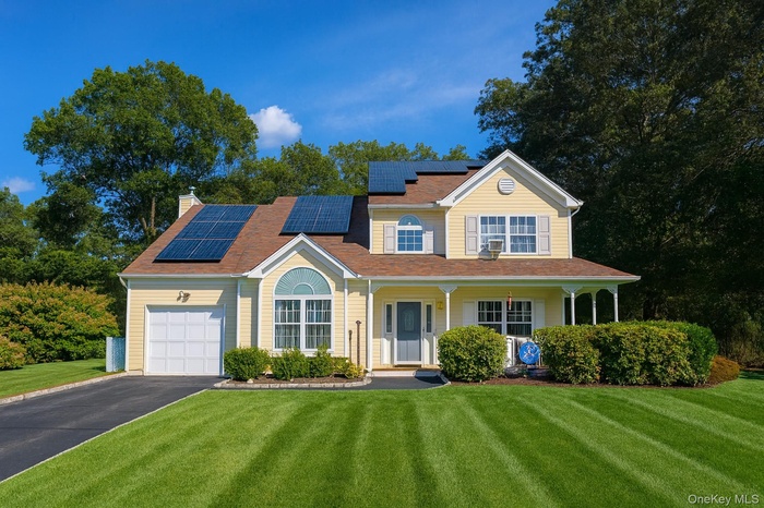 View of front of house with roof mounted solar panels, a porch, driveway, and a chimney