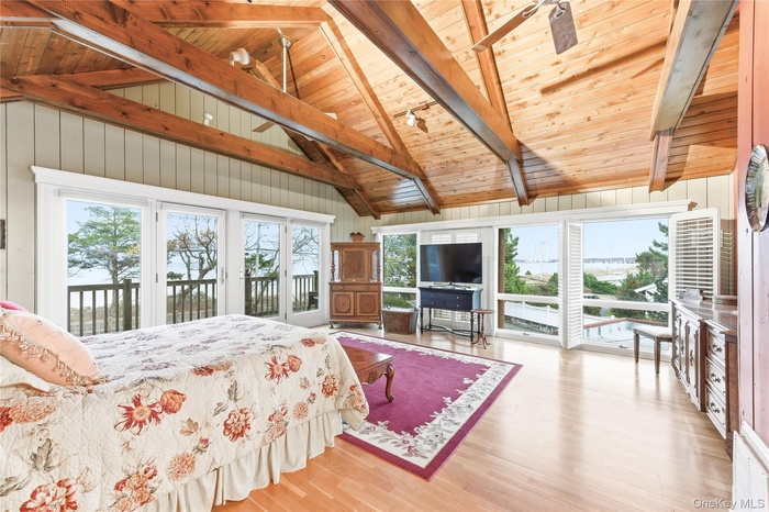 Bedroom with access to exterior, multiple windows, light wood finished floors, a wood ceiling with exposed beams, and wood walls