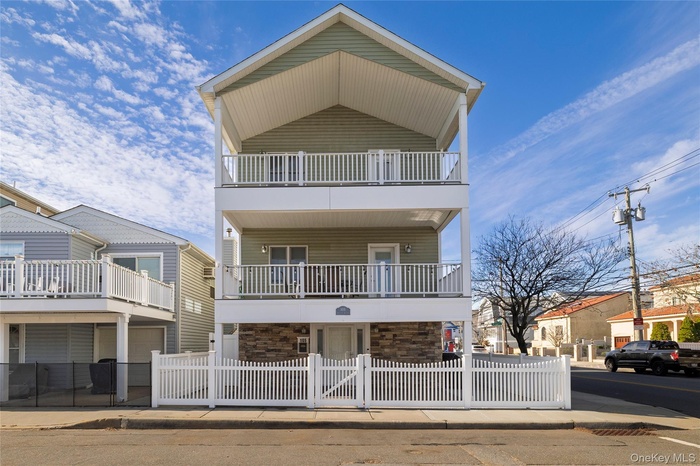View of front of property featuring a fenced front yard, stone siding, and a balcony