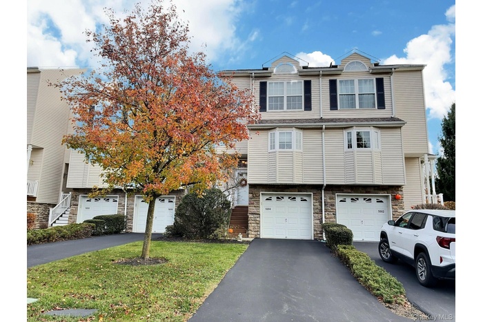 View of front of house featuring stone siding, driveway, an attached garage, and a front lawn