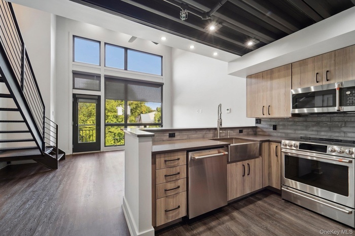 Kitchen with appliances with stainless steel finishes, a peninsula, dark wood finished floors, backsplash, and rail lighting