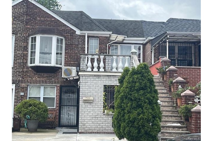 View of front of home featuring brick siding, roof with shingles, a balcony, and stairs