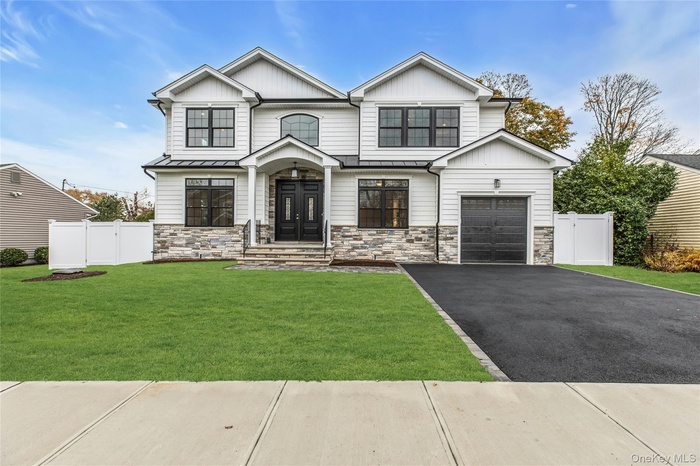 View of front of house with stone siding, driveway, a garage, board and batten siding, and a standing seam roof