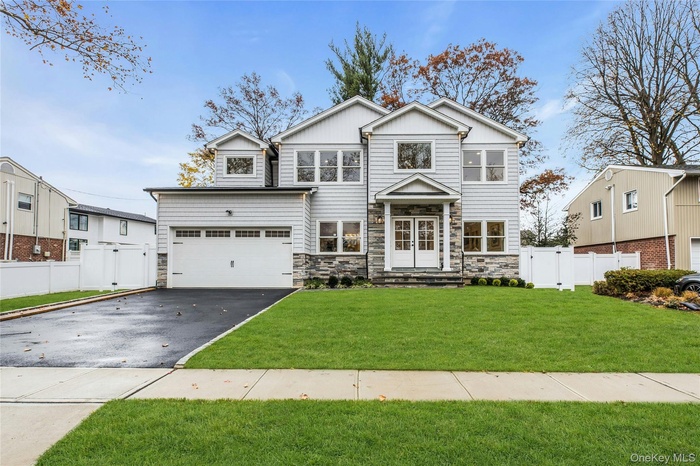 View of front of property with asphalt driveway, stone siding, a gate, and an attached garage