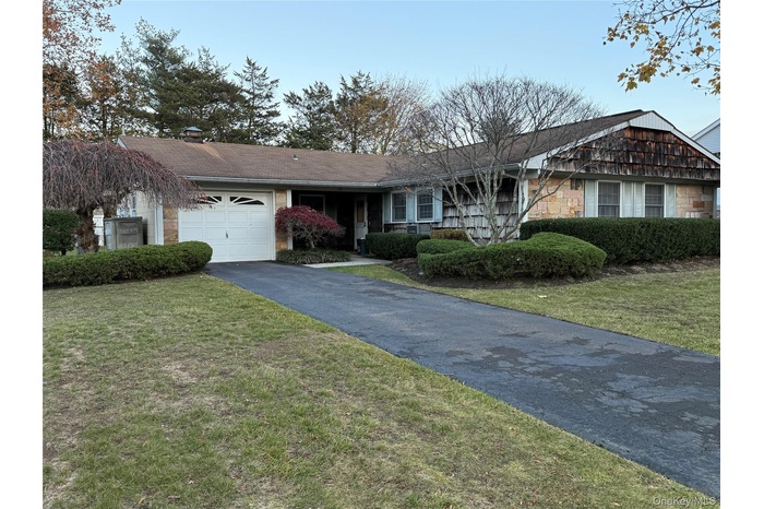 Single story home with driveway, a front lawn, stone siding, a chimney, and a garage