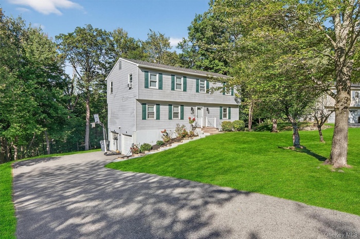 Colonial-style house with driveway, a front lawn, a garage, and view of wooded area
