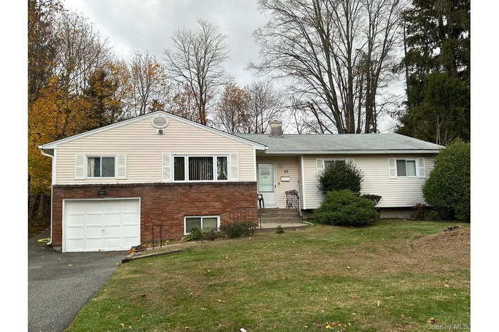 View of front of home with brick siding, a front lawn, driveway, and a chimney