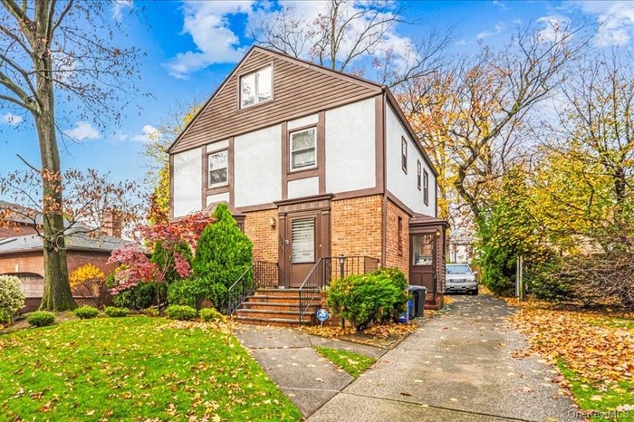 Tudor home featuring brick siding, stucco siding, a front lawn, and concrete driveway