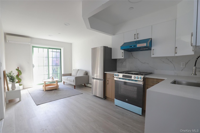 Kitchen with appliances with stainless steel finishes, under cabinet range hood, backsplash, light wood-style flooring, and white cabinetry