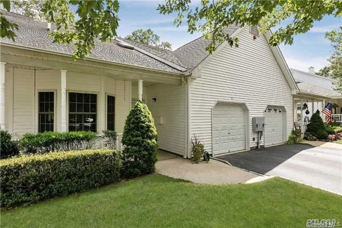 View of side of home with covered porch, asphalt driveway, a yard, an attached garage, and a shingled roof
