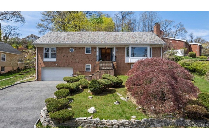 View of front of house with asphalt driveway, brick siding, a chimney, and a garage
