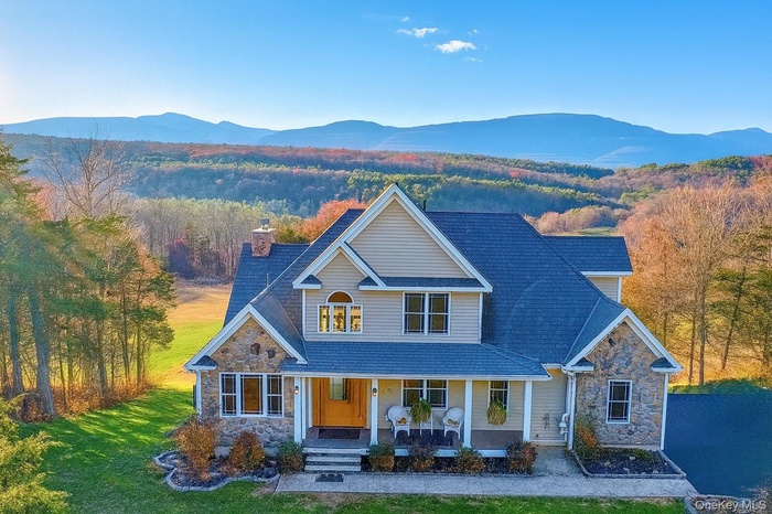 View of front of house with stone siding, covered porch, a chimney, a forest view, and a front yard