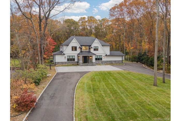 Modern farmhouse with a porch, a front yard, stone siding, and asphalt driveway