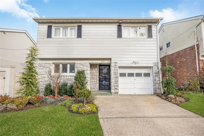 View of front of property featuring stone siding, an attached garage, driveway, and a front yard
