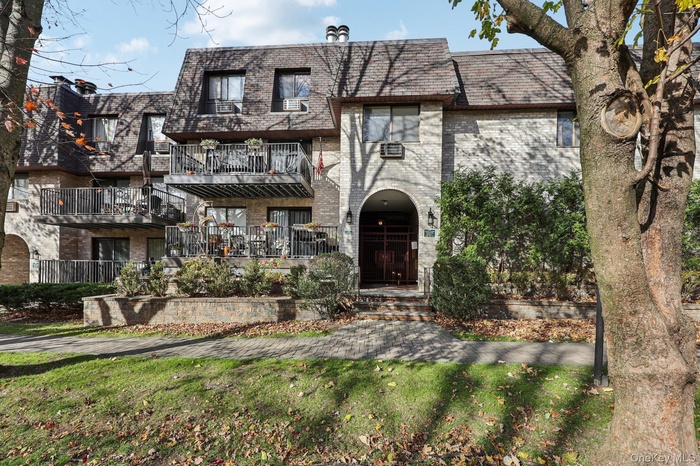 View of front of house featuring mansard roof, brick siding, and a balcony