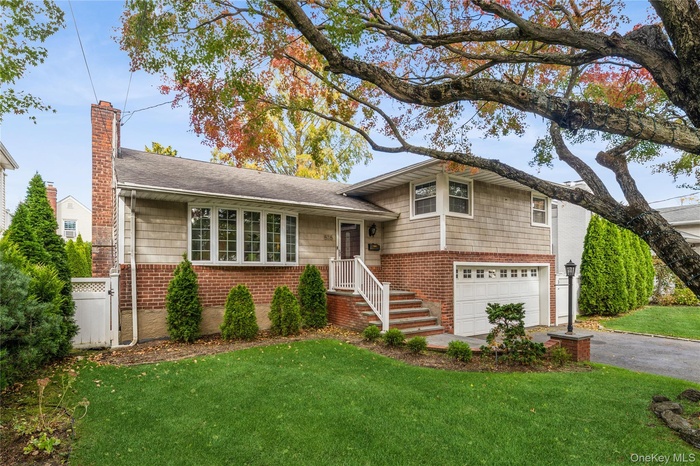 Split level home featuring, asphalt driveway, brick siding, a chimney, and a shingled roof