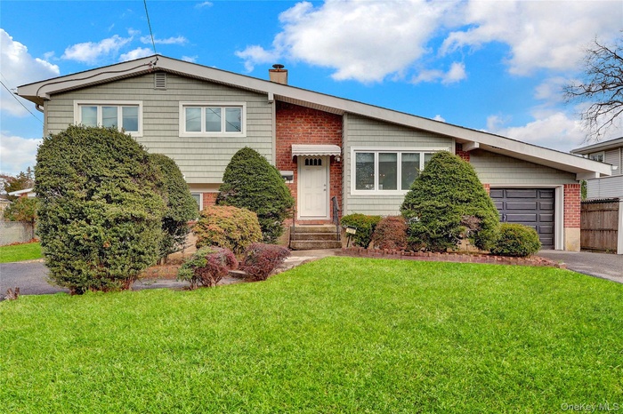 View of front of property with a front yard, a chimney, a garage, and asphalt driveway