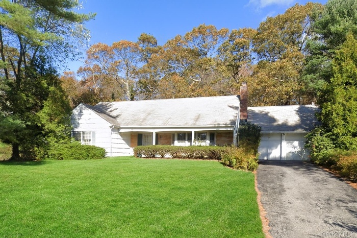 Ranch-style home featuring a front lawn, a chimney, driveway, an attached garage, and covered porch