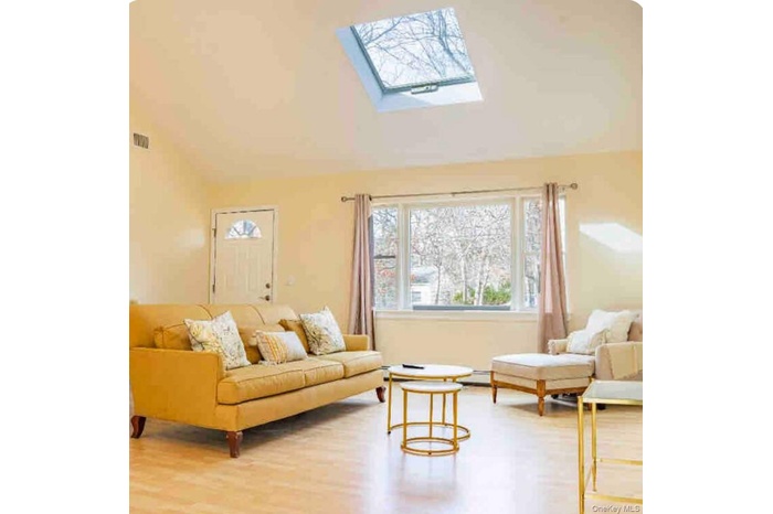 Living area featuring a skylight, vaulted ceiling, and light wood-style flooring