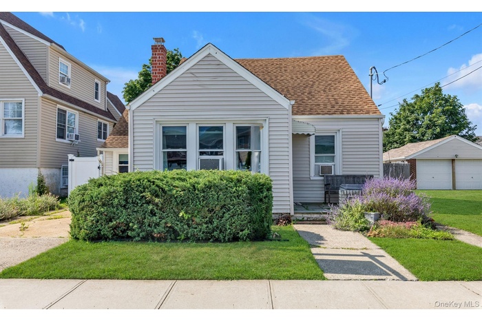 View of front of house featuring a chimney, a front yard, roof with shingles, a garage, and an outdoor structure