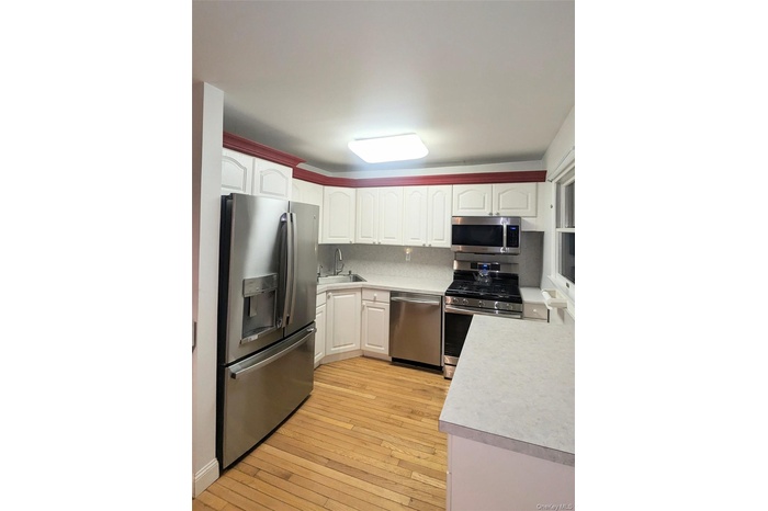Kitchen featuring appliances with stainless steel finishes, light countertops, light wood-type flooring, and white cabinetry