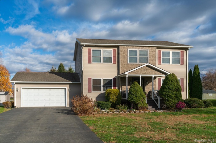 Traditional-style home featuring an attached garage, driveway, a front lawn, and roof with shingles