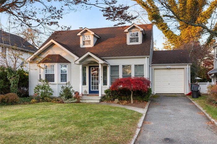 Cape cod house with a front yard, driveway, a shingled roof, and a garage