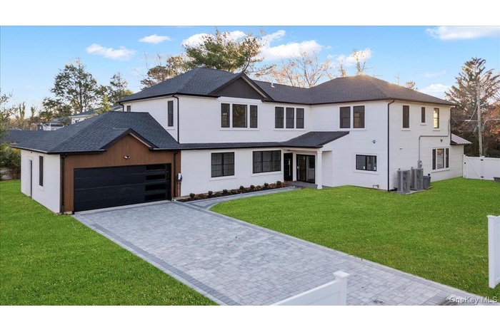 Modern farmhouse with a front yard, decorative driveway, and an attached garage