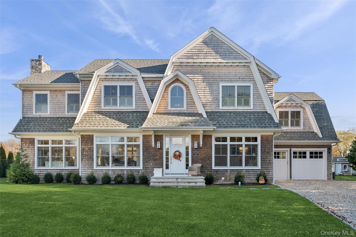 Shingle-style home featuring a gambrel roof, a shingled roof, a chimney, a front yard, and a garage