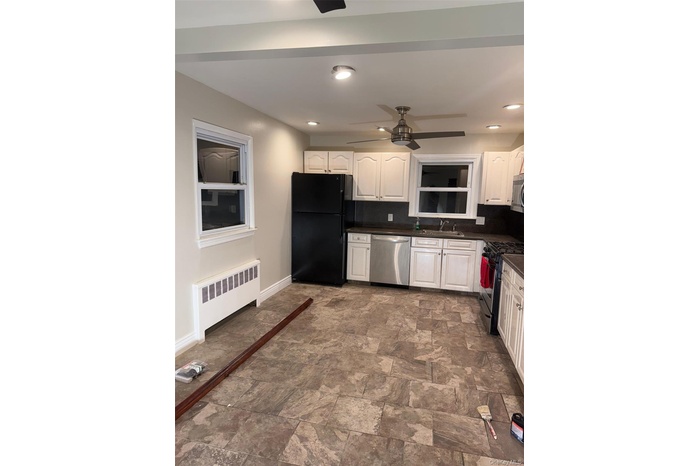 Kitchen featuring white cabinetry, stainless steel appliances, stone finish flooring, radiator, and recessed lighting