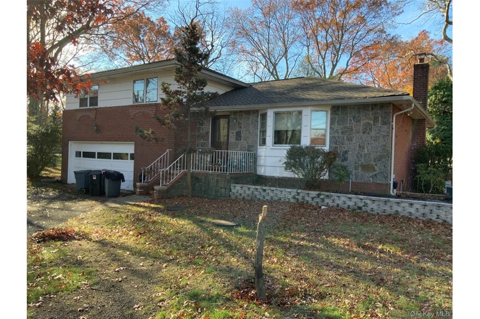 Split level home featuring a chimney, stone siding, an attached garage, and driveway
