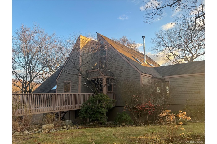 Back of property with a deck, a shingled roof, and a lawn