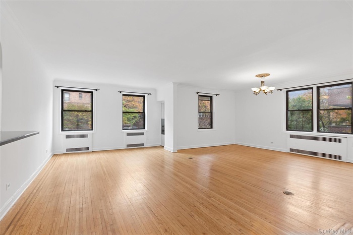 Unfurnished living room featuring radiator heating unit, light wood finished floors, and a chandelier