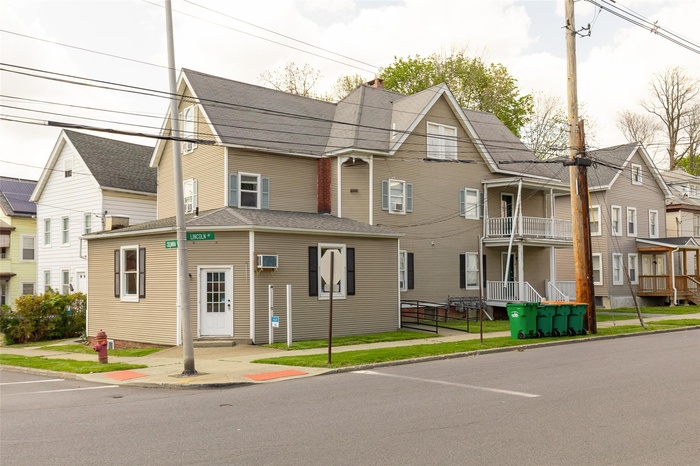 View of front facade with a chimney, a wall unit AC, and a shingled roof