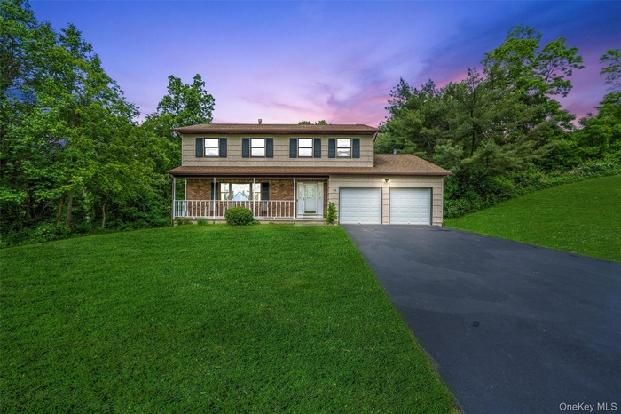 Traditional-style house with driveway, a front yard, a porch, and an attached garage