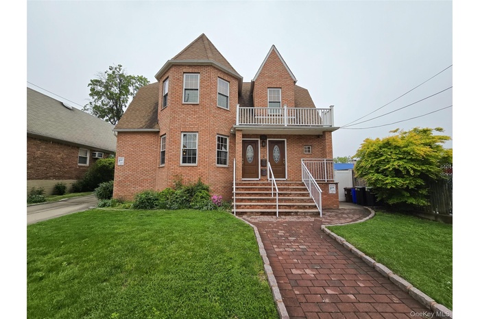 View of front of house with brick siding, a front lawn, a balcony, and roof with shingles