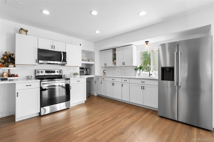 Kitchen with stainless steel appliances, light countertops, white cabinets, open shelves, and recessed lighting