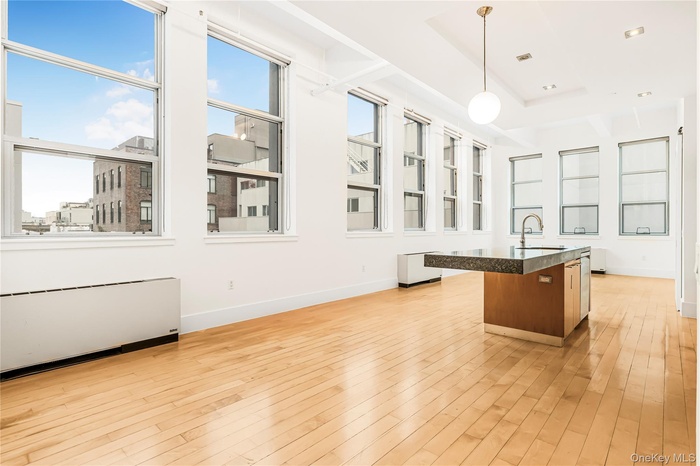 Kitchen featuring radiator, hanging light fixtures, light wood-style flooring, a kitchen island with sink, and glass insert cabinets