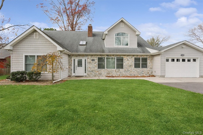 View of front of property featuring a front yard, roof with shingles, an attached garage, asphalt driveway, and a chimney