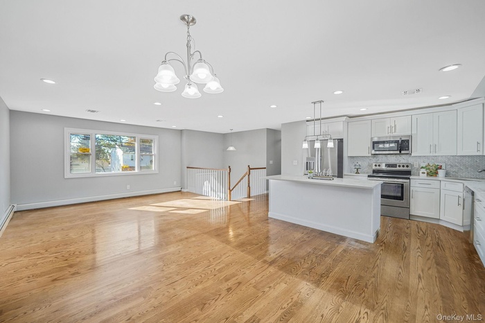 Kitchen with decorative light fixtures, white cabinetry, open floor plan, appliances with stainless steel finishes, and a kitchen island